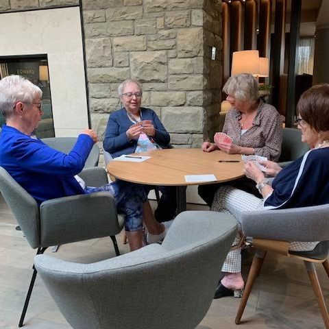 Four senior women sitting at a round table together playing a game of cards.