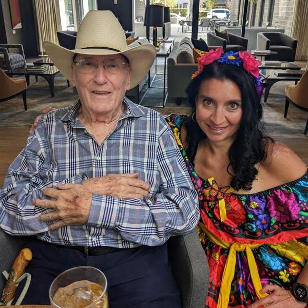 A senior man in a cowboy hat posing for a picture with a women in Cinco de Mayo clothing.