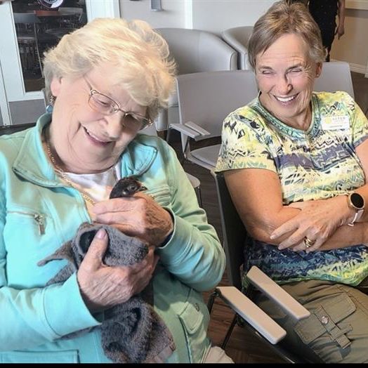 Senior women seated together smiling. One of the women is holding a bird gently.