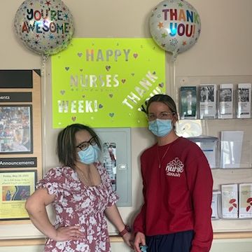 Two nurses standing in front of a sign that says, 