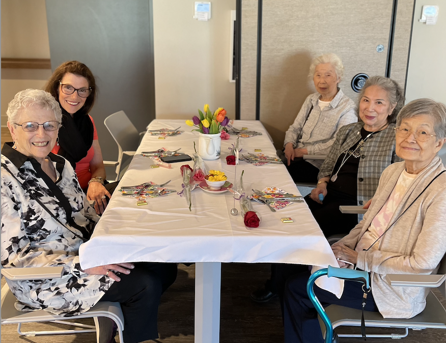 Senior women seated together smiling at a set table. There are multiple coloured tulips in the middle of the table.