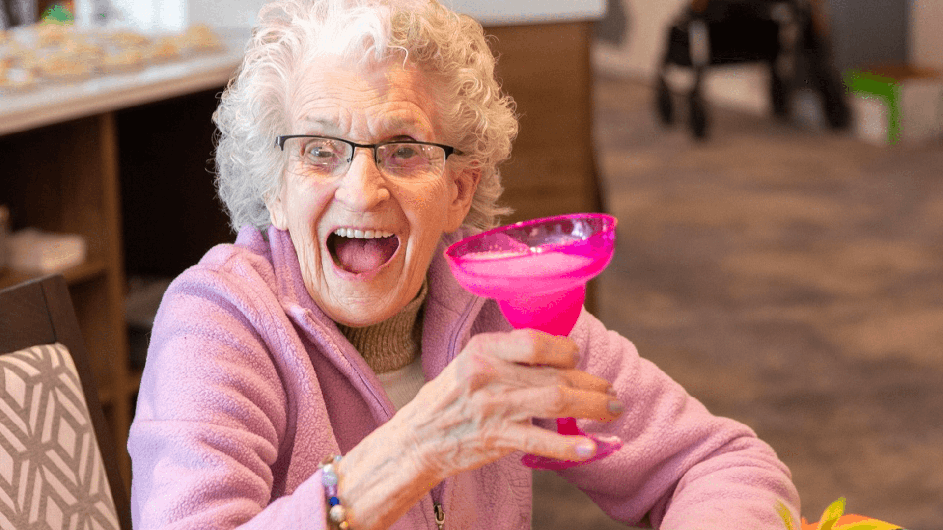 Senior lady smiling holding a cocktail in a pink cup