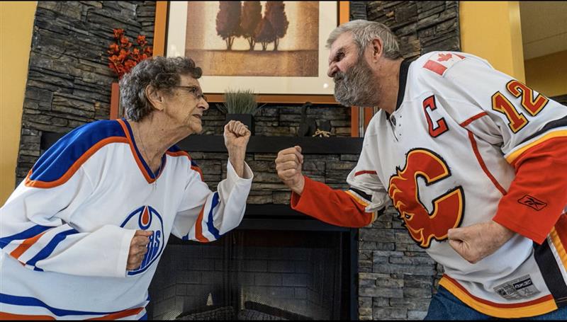 Two seniors pretending to be aggressive to each other. One is wearing an Edmonton Oilers jersey, and the other is in a Calgary Flames jersey.