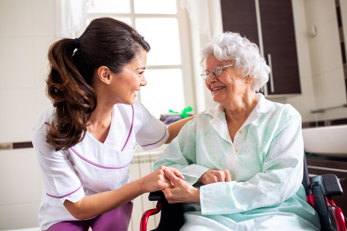 A young brunette nurse holding an elderly woman's hand in long-term care