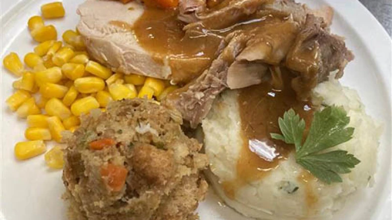 Thanksgiving plate featuring mashed potatoes, stuffing, corn, carrots, turkey, and gravy.