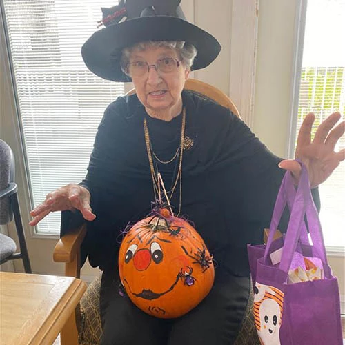 Resident making a spooky expression in a witch costume while holding a decorated pumpkin and a bag of candy.
