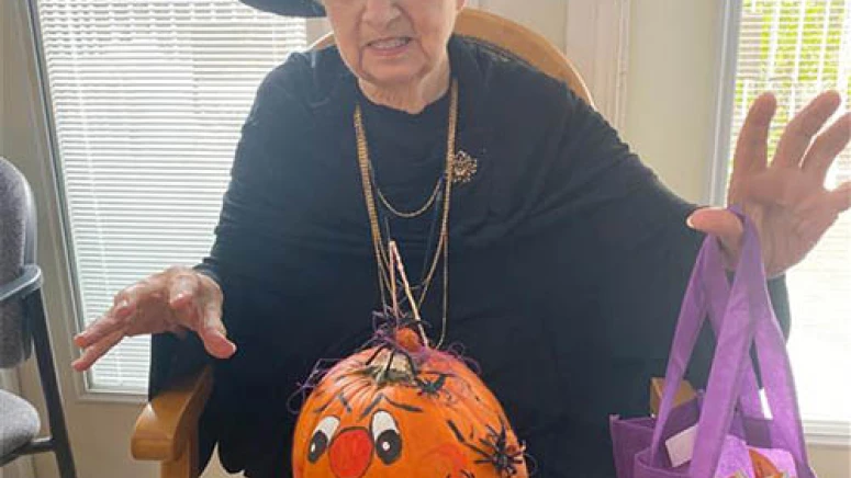 Resident making a spooky expression in a witch costume while holding a decorated pumpkin and a bag of candy.