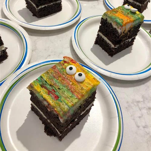 Halloween cake on a table for residents. It is chocolate cake with yellow, green, and red icing blended. The cake also has spooky candy eyes on it.