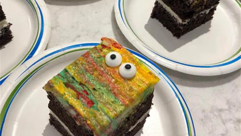 Halloween cake on a table for residents. It is chocolate cake with yellow, green, and red icing blended. The cake also has spooky candy eyes on it.