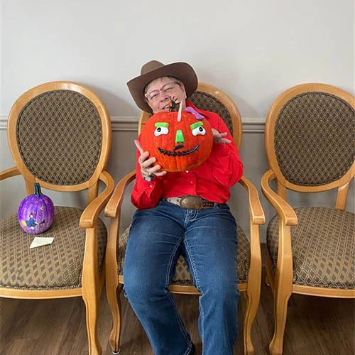 Resident smiling while holding a pumpkin and wearing a cowgirl costume.