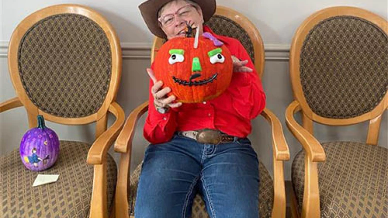 Resident smiling while holding a pumpkin and wearing a cowgirl costume.