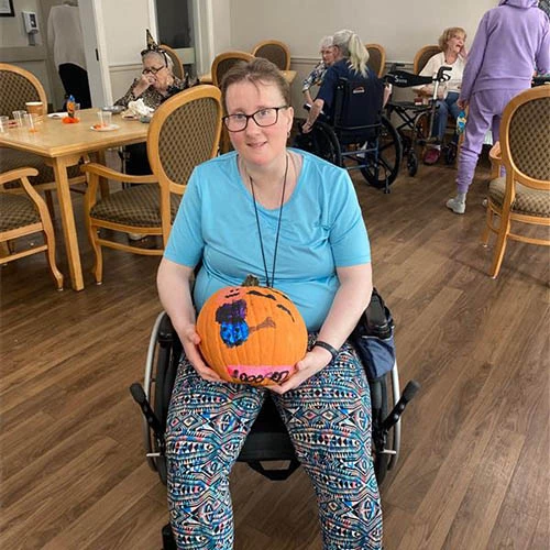 Resident smiling and sitting while holding a pumpkin.