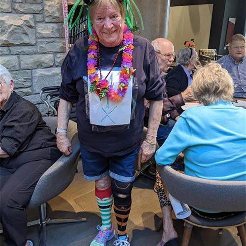 Resident in a goofy Halloween costume. She is smiling while wearing colourful socks, a Hawaiian Lei and a silly wig.