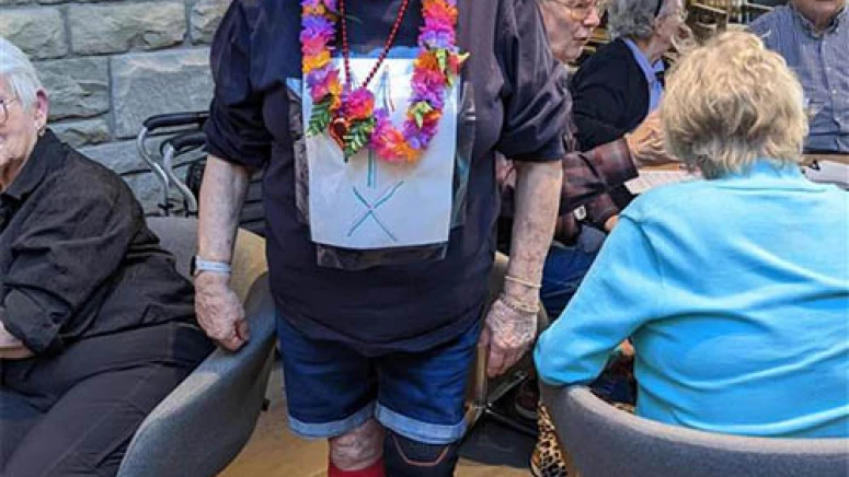 Resident in a goofy Halloween costume. She is smiling while wearing colourful socks, a Hawaiian Lei and a silly wig.