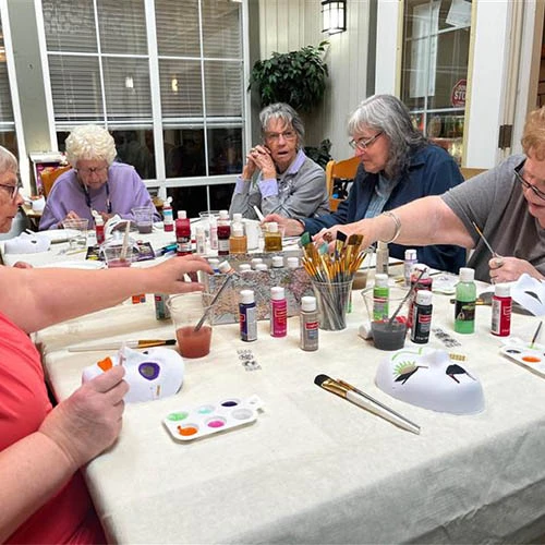 Residents surrounding a table together painting masks and enjoying each other's company.