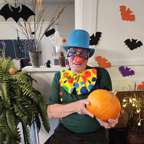 Resident dressed in a clown costume for Halloween. He is smiling and holding a pumpkin.