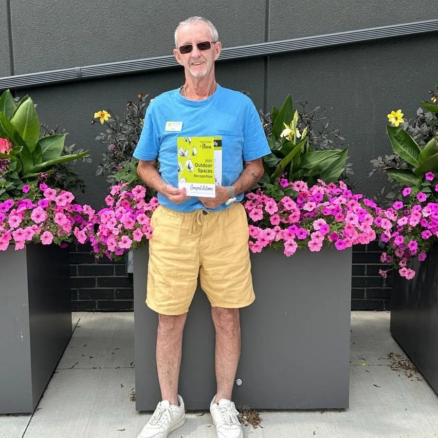 Senior man standing in front of flowers holding an award recognition card