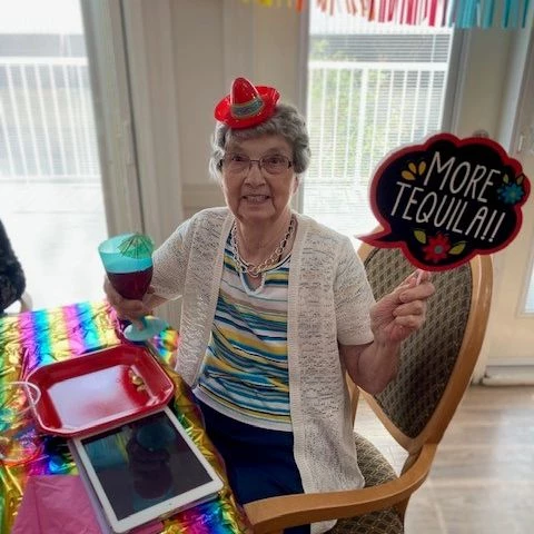 A senior resident posing with Cinco de Mayo decorations. She is holding a drink and a sign that says, 