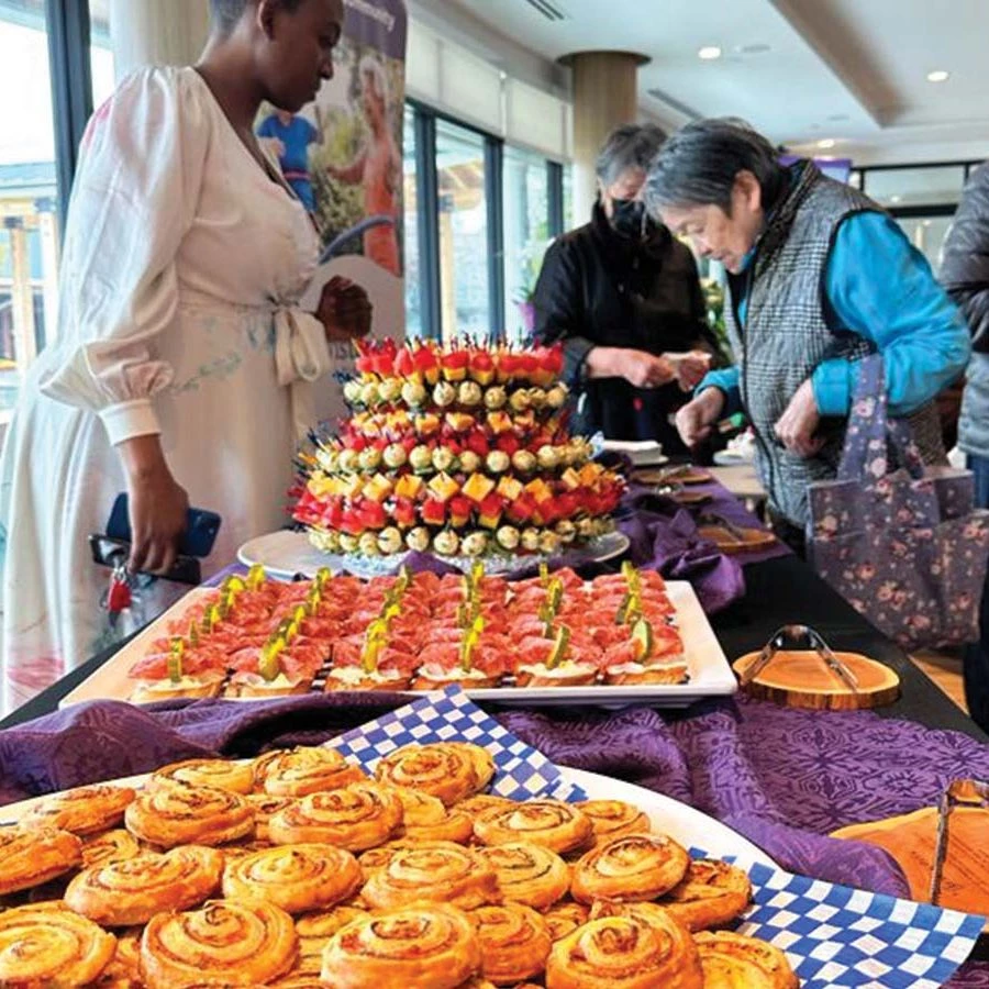 Table full of stacks of food. Cinnamon buns, pastries, and kabobs on platters are placed on the purple tablecloth.