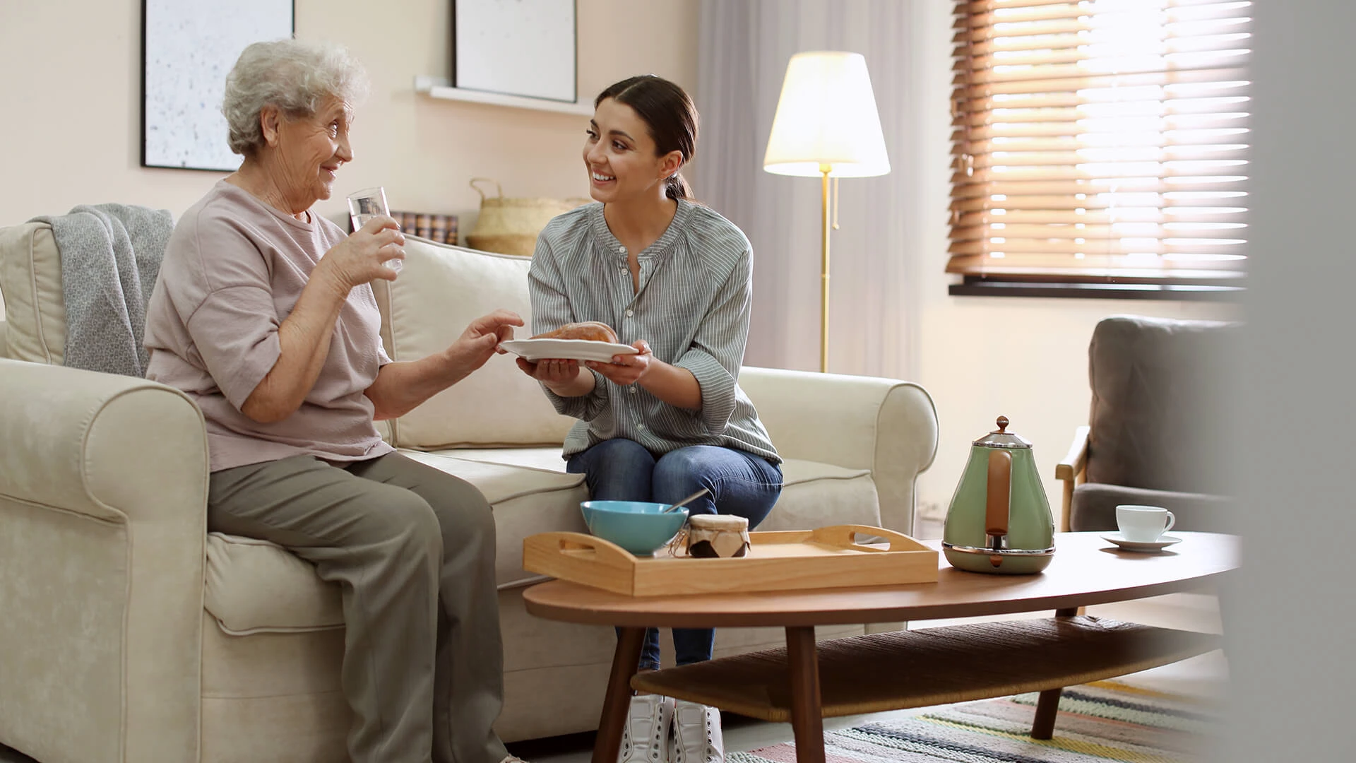 A young lady serving breakfast to an elderly woman in a senior apartment