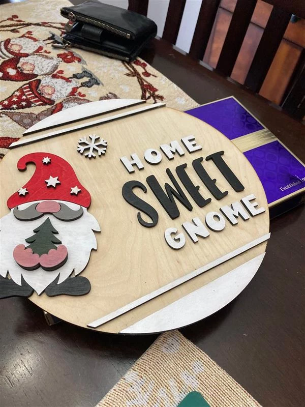 Christmas decoration on a round piece of wood. There is a gnome with a christmas hat on the sign with the words, 