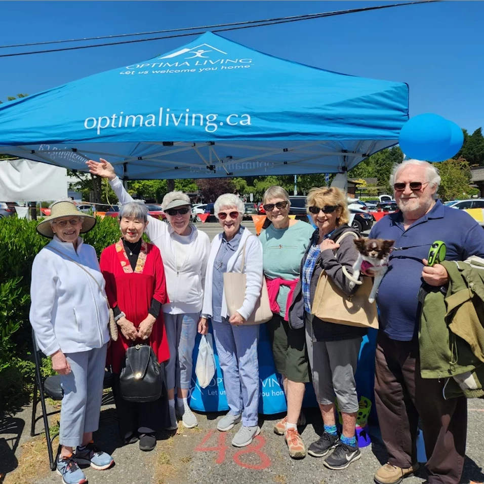 Seniors standing outside with the Optima Living tent behind them