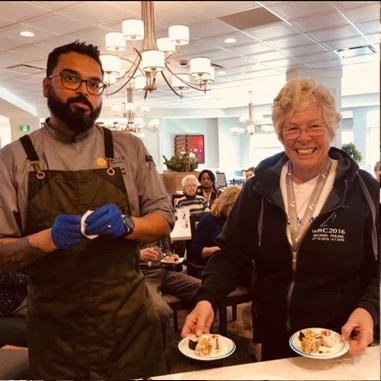 Aster Gardens chef standing next to a senior holding two plates of dessert