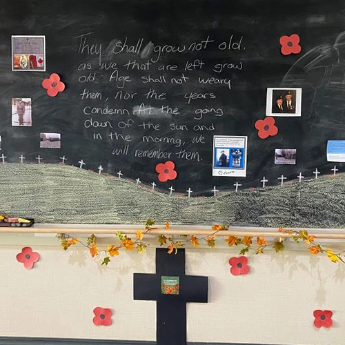 Remembrance day display featuring a poem, photos, poppies, and a cross.