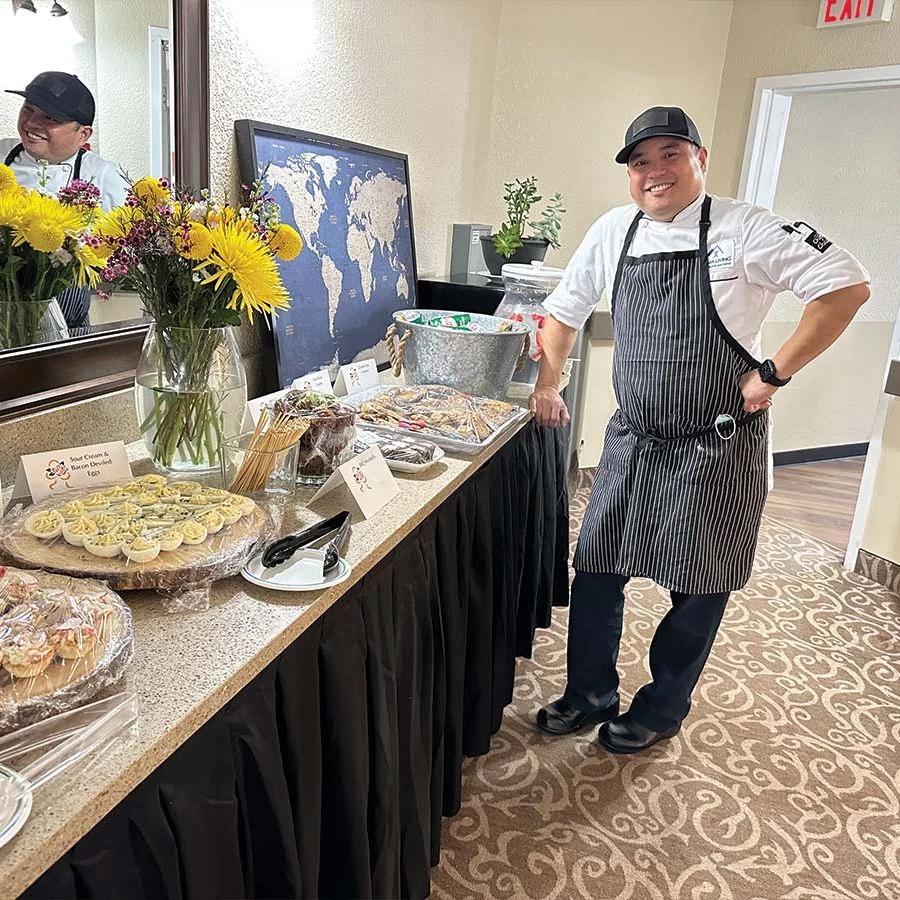Chef Scott smiling and standing proudly in front of a table full of delicacies he has prepared.