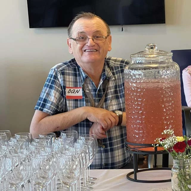 Senior man smiling next to a jar of punch. He has a name tag that reads, 
