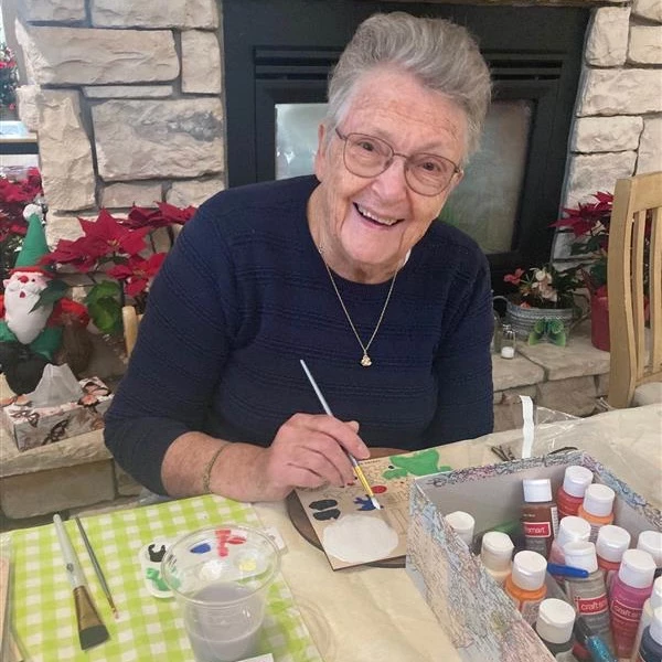 A senior woman smiling while painting and doing some Christmas crafts.