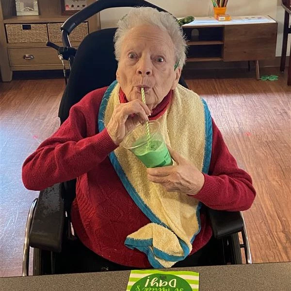 A senior enjoying a green milkshake. She is wide-eyed and seems to be enjoying it!