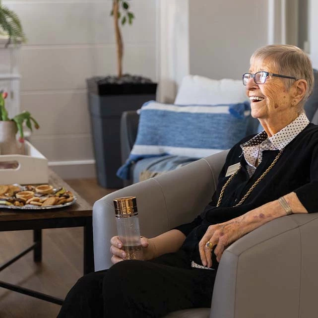 Senior woman in a chair laughing while holding sparkling water