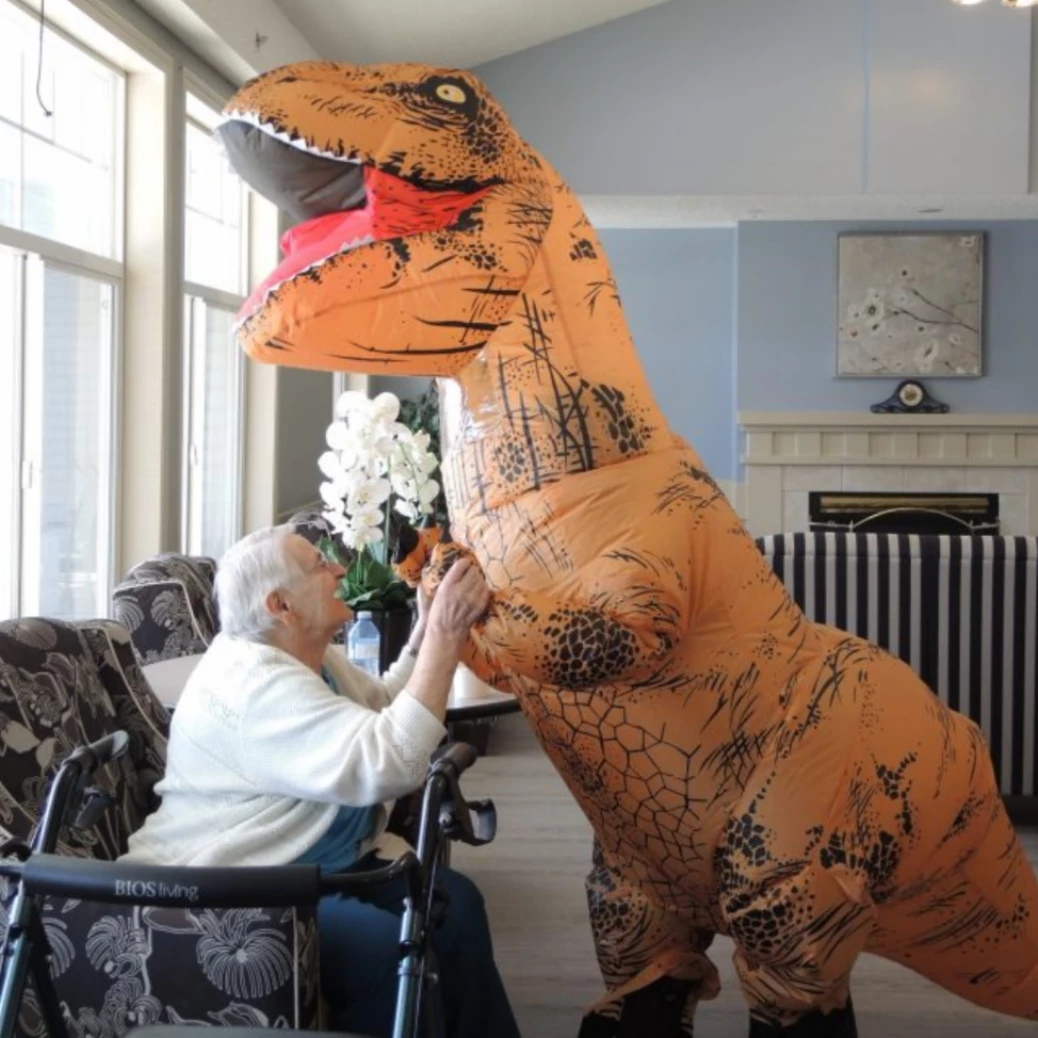 Giant inflatable dinosaur costume holding hands with a senior resident.