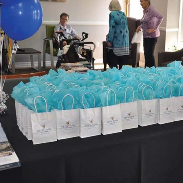 Gift bags with teal tissue paper on a table during the open house. The bags have the Deer Park Village log on them.