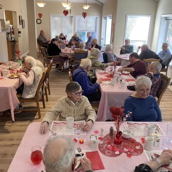 Seniors seated together at a Valentine's day dinner. The tables are decorated with pink tablecloths and heart decorations.